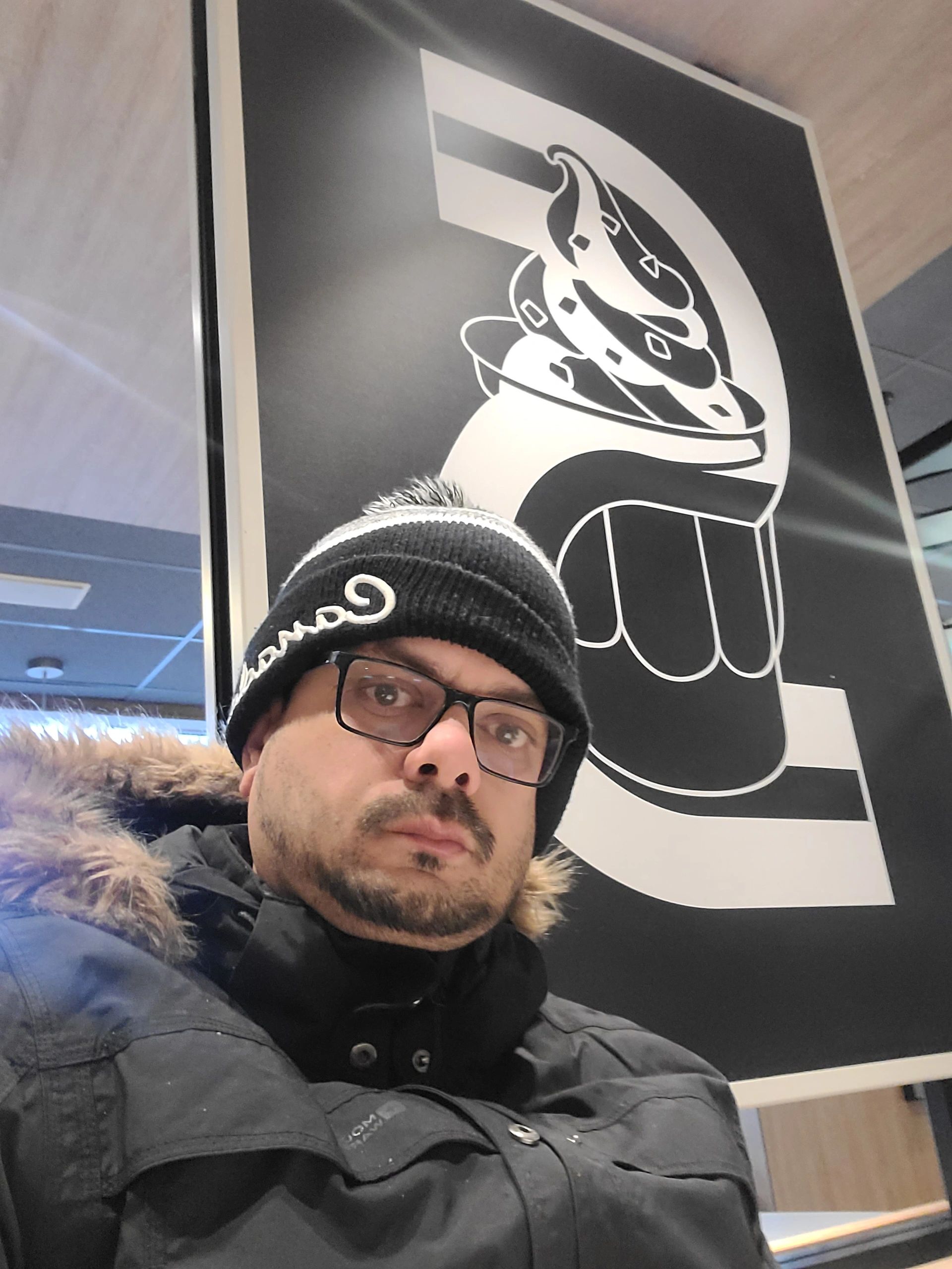 Man in winter coat and beanie in front of abstract black and white art.