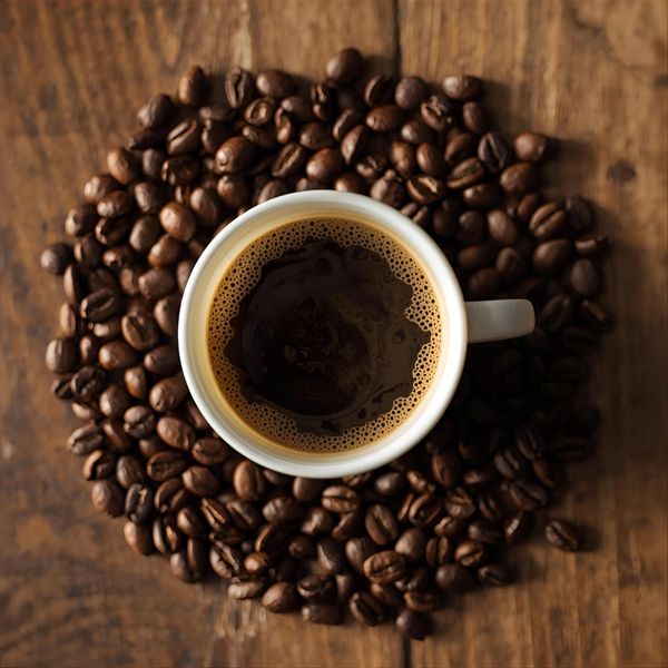 Top view of a coffee cup surrounded by coffee beans on wood.