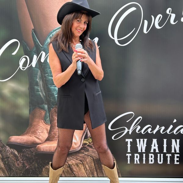 Woman in cowboy hat holding microphone with Shania Twain tribute backdrop.