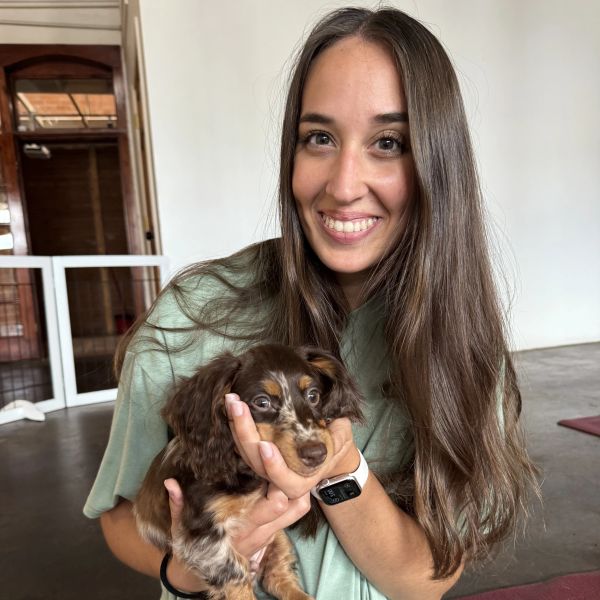 Young woman smiling while holding a small brown puppy.
