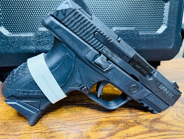 Black Ruger handgun with a white band on the grip, placed on a wooden surface.