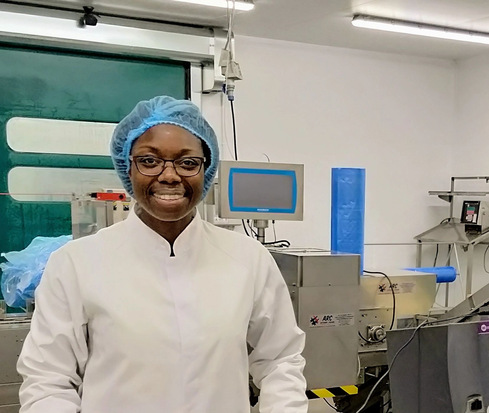 Barbara stands in a vegetable packhouse dressed in a white protective clothing and a blue hairnet.