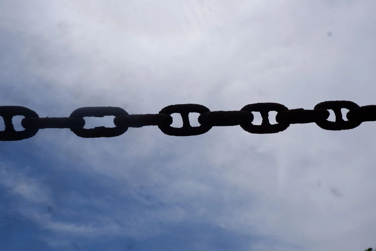 Close-up silhouette of a rusty chain against a cloudy sky.