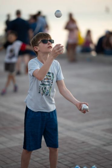 Boy juggling two white balls outdoors.