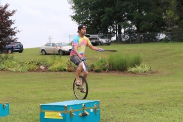Man riding a unicycle outdoors on a grassy field.