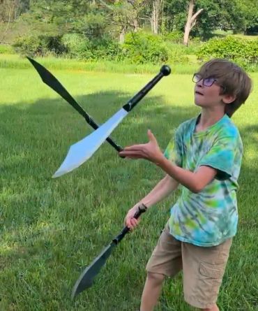 Boy juggling three swords outside.