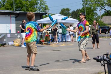 Two people juggling outdoors wearing tie-dye shirts.