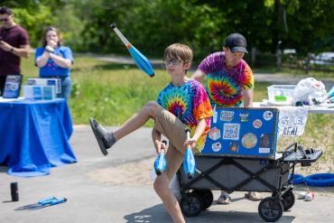 Boy juggling clubs outdoors in colorful tie-dye shirt.