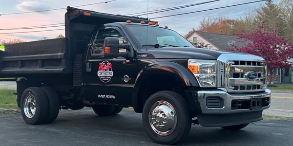 Black Ford dump truck with KP Contracting logo parked on driveway.