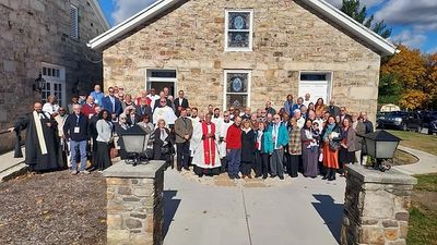 Large group gathered outside a stone church on a sunny day.