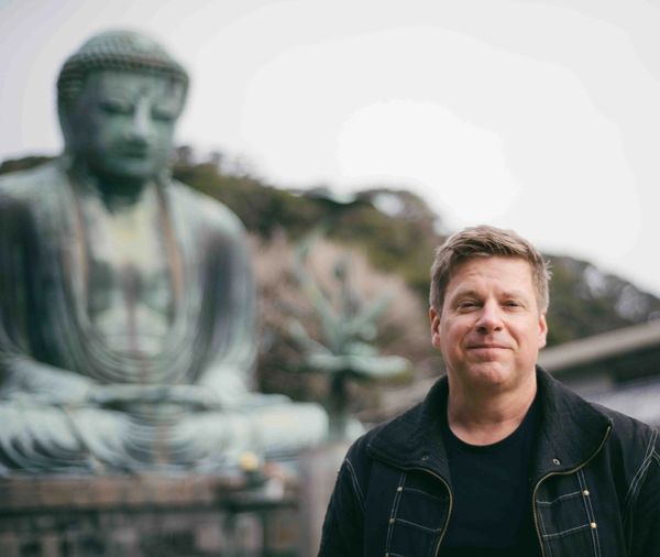 Man standing near a large Buddha statue outdoors.