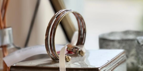 Decorative ceramic box with bangles and a ribbon on top, surrounded by plates and reed diffuser sticks.