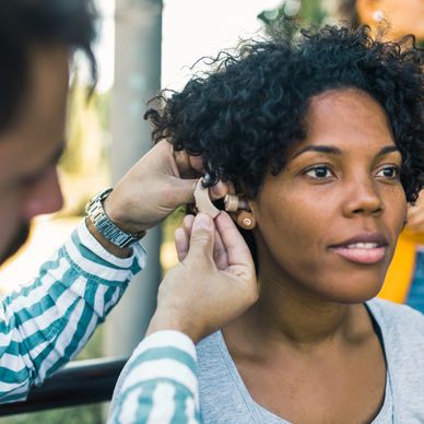 Man fitting a hearing aid in a woman's ear outdoors.