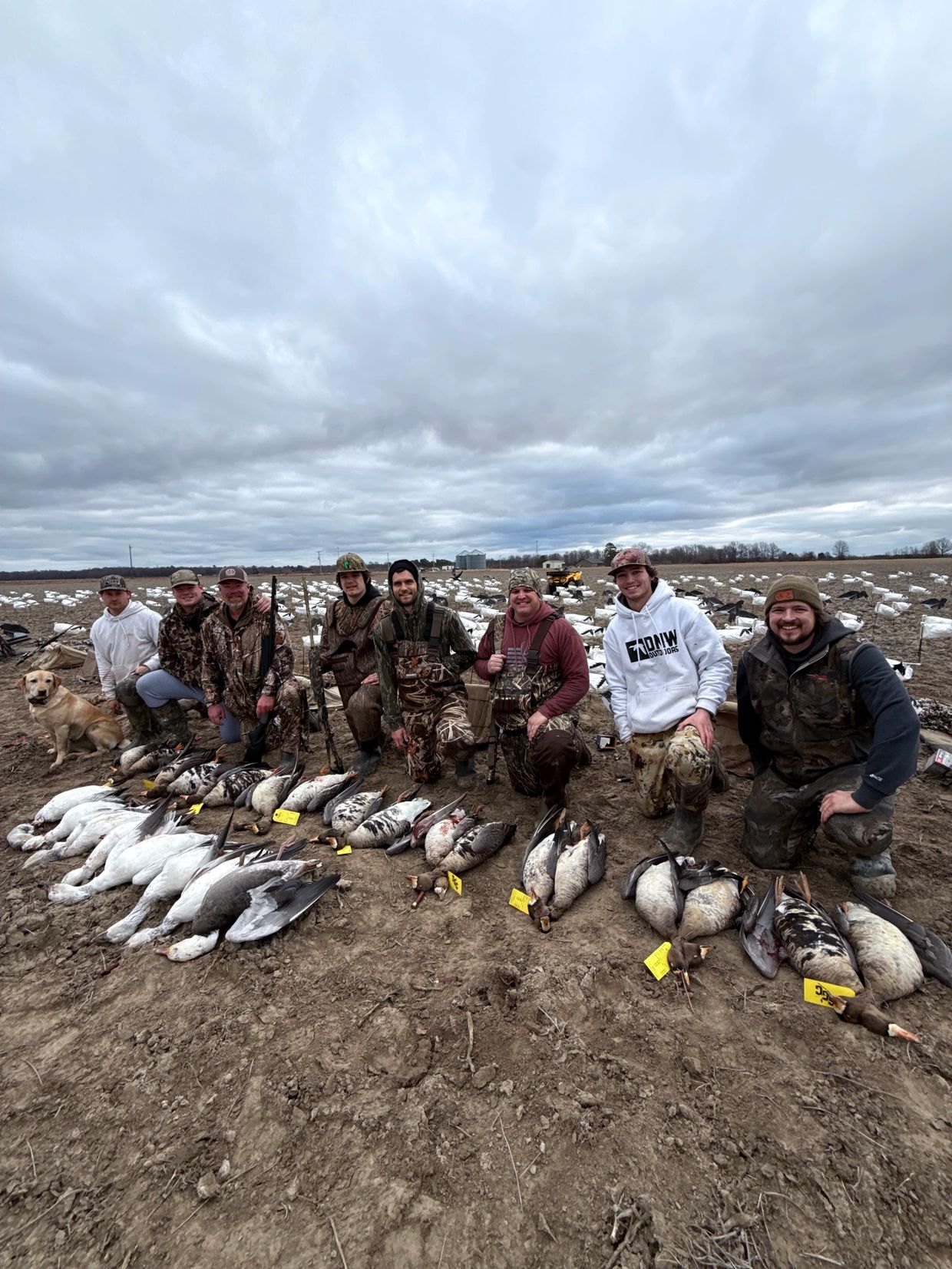 Group of hunters posing with their waterfowl and hunting gear in a field.