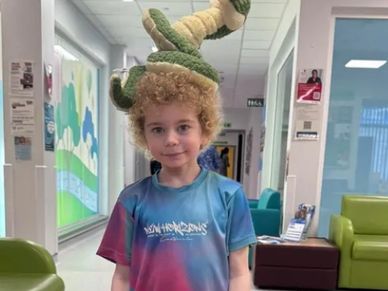 A child wearing a plush crocodile hat in a colorful shirt inside a hallway.