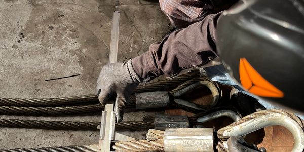 Workers measuring steel wire rope with calipers for safety.