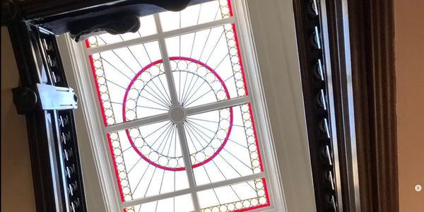 Looking up through a staircase at a decorative stained glass ceiling window.