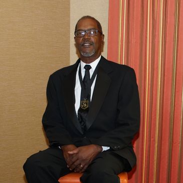 Man in black tuxedo sitting on a stool with a medal.