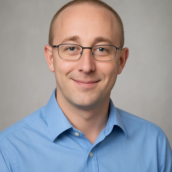 Smiling man wearing glasses and a blue shirt against a neutral background.
