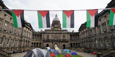 Palestinian flags hang above tents set up in a historic courtyard.