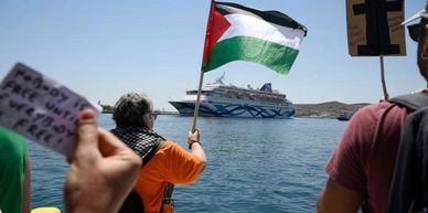 Protesters by the sea, one waving a Palestinian flag near a docked cruise ship.