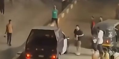 People gather near a black car on a roadside at night.
