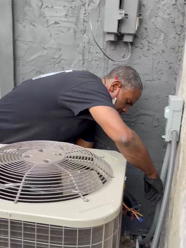 Technician repairing an air conditioning unit outside a building.