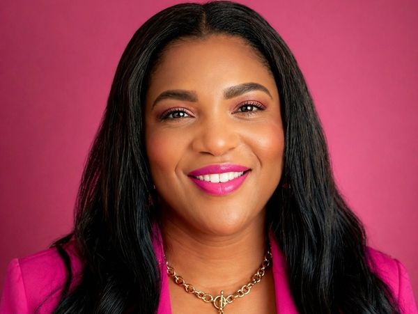 Smiling woman with long black hair and pink lipstick against a magenta background.