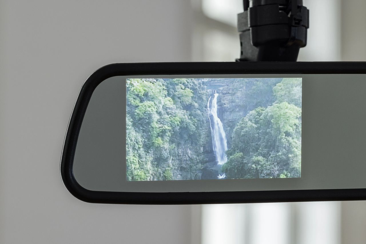A rearview mirror displaying a scenic waterfall surrounded by lush green trees.