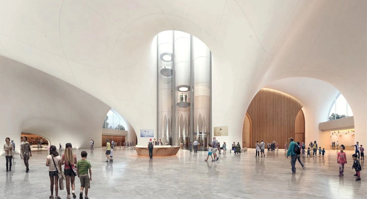 An interior view of a modern architecture space, featuring high, curved ceilings and large glass panels. People are gathered, including families and individuals, exploring the spacious area with a central reception desk and visible elevators.