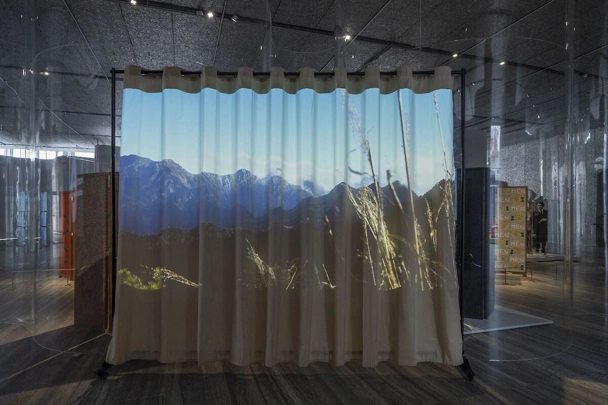 A projection of mountains and grass displayed on a curtain in a modern gallery space.
