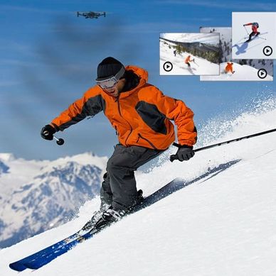 Skier in orange jacket skiing down a snowy mountain with drone capturing footage.