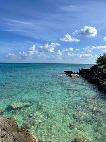 Clear turquoise sea with rocky shores under a partly cloudy blue sky.