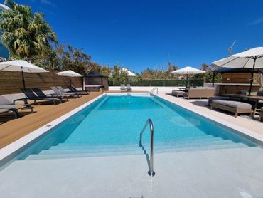 A modern outdoor swimming pool with lounge chairs and umbrellas under clear blue sky.