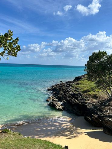 A serene beach with turquoise water and rocky coastline under a blue sky.