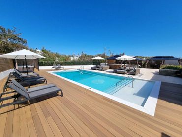Modern outdoor pool area with sun loungers and umbrellas under clear blue sky.