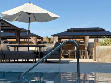 Modern outdoor pool area with cabanas and umbrella seating under clear blue sky.