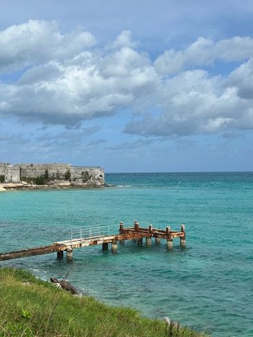 A rustic pier extends into clear turquoise waters under a cloudy sky.