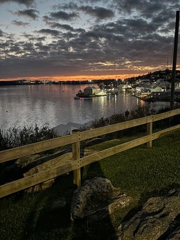 Sunset over a calm harbor with lights reflecting on the water.