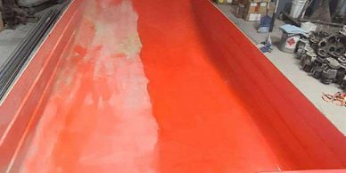 A large red boat hull inside a workshop, partially sanded.