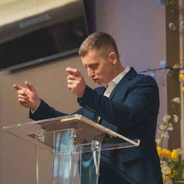 Man in suit speaking passionately at a clear podium indoors.