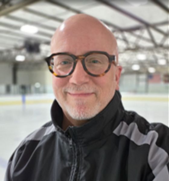 Smiling man wearing glasses at an ice rink.