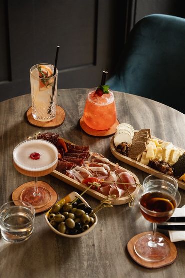 A table with cheese and meat boards surrounded by cocktails