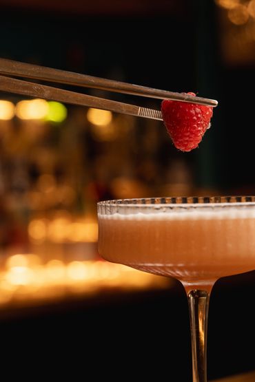 A raspberry being places on a Martini cocktail