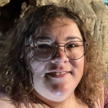 Close-up of a woman smiling with glasses and curly hair.