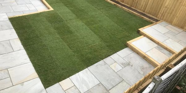 Sandstone patio and laid turf with fencing and retaining sleepers