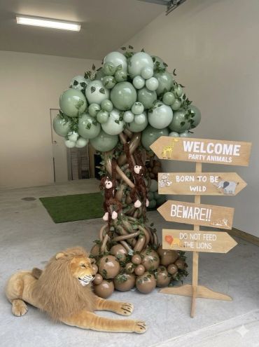 Decorative jungle-themed setup with a balloon tree, wooden sign, and a plush lion.