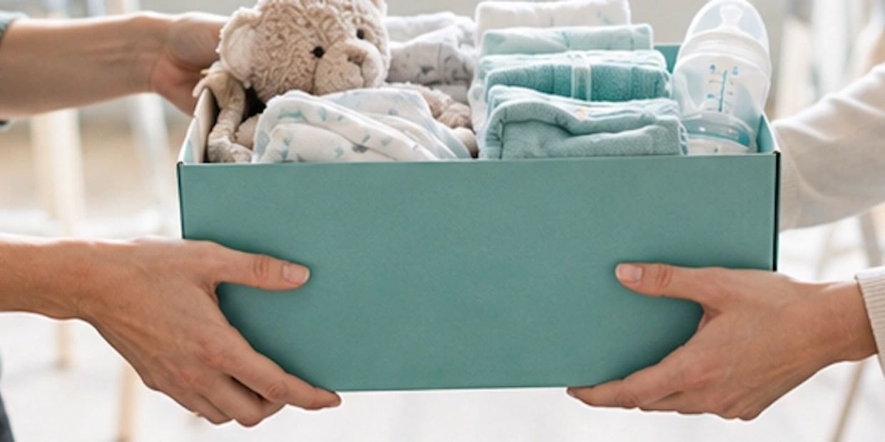 Two hands holding a blue box filled with baby essentials.