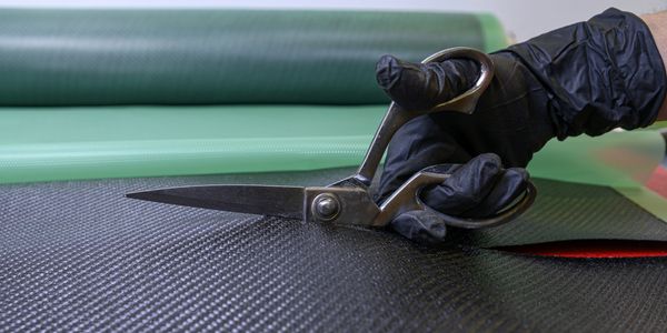 Hand with black glove cutting carbon fiber fabric with scissors.