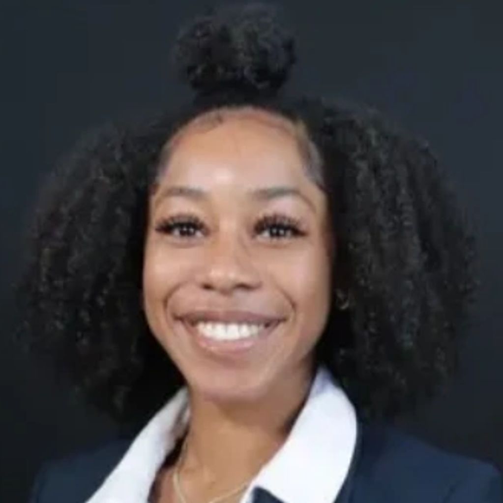 Young woman in formal blazer smiling against a dark background.